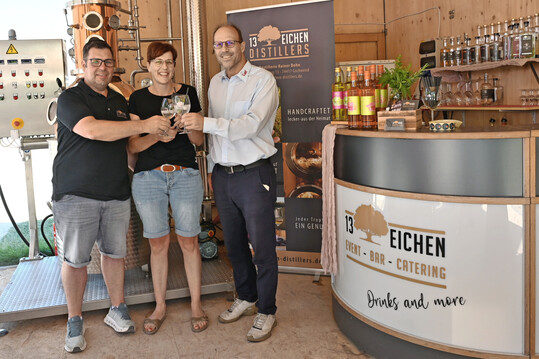 Rainer und Anja Bohn stoßen mit Alexander Plank von der Firma Carl vor deren Schaubrennerei im Pavillon der Landesgartenschau Ellwangen an.