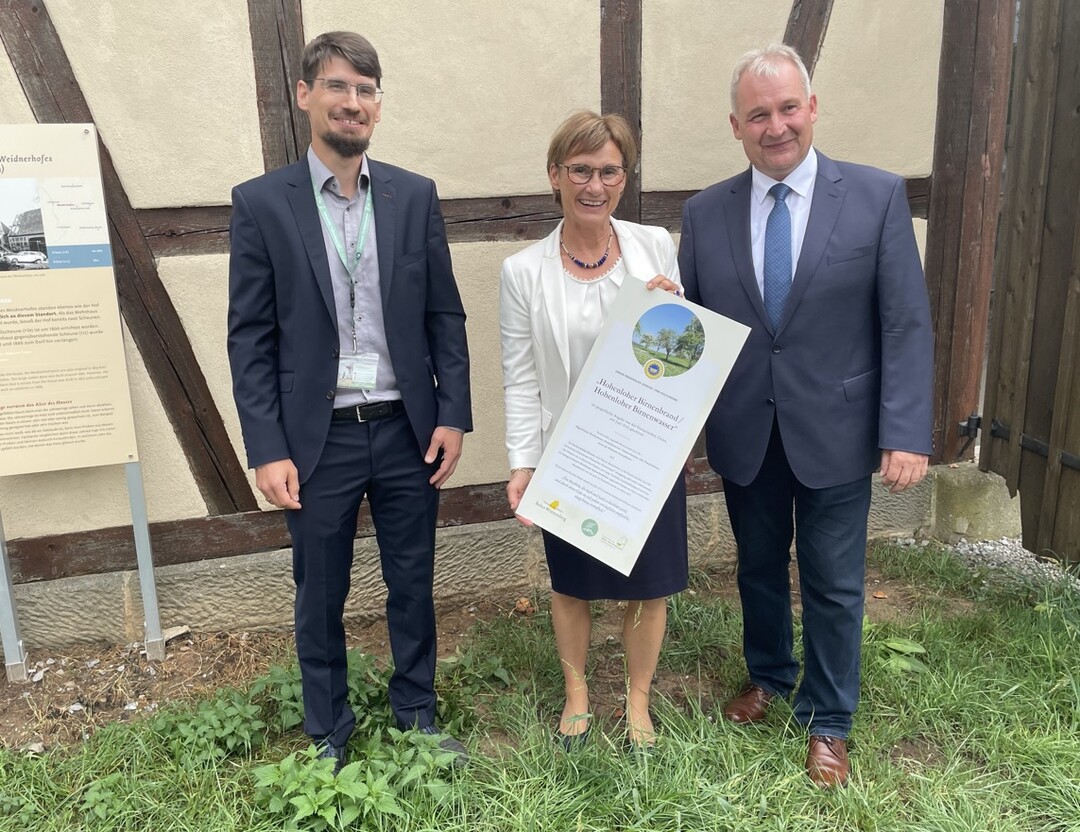 Bernd Beck, der stellvertretende Leiter des Hohenloher Freilandmuseums Schwäbisch Hall-Wackershofen, Sabine Kurtz, Staatssekretärin im Ministerium für Ernährung, Ländlichen Raum und Verbraucherschutz und Karl Müller, 1. Vorsitzender des Landesverbandes der Klein- und Obstbrenner Nord-Württemberg e. V. mit dem Schild zum Hohenloher Birnenbrand, das in der Museumsbrennerei angebracht werden wird.