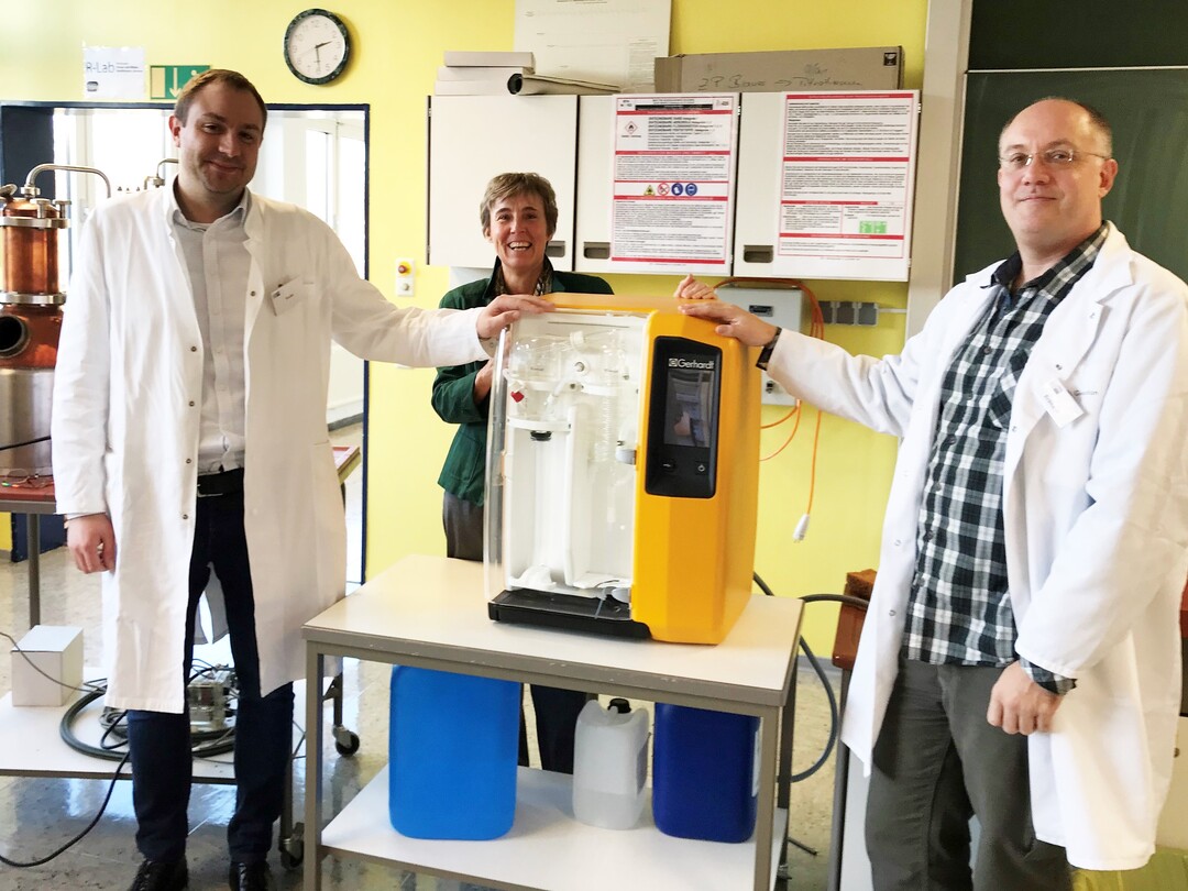 Freudestrahlend nimmt Abteilungsleiterin Sabine Droste, FHBK , (2.v.l.) das Schnelldestilliergerät von Senior Flavourist Johannes Roder, Hertz&Selck, (1.v.l.) und Schriftführer Martin Erdmann, Vereinigung der Destillateurmeister, (3.v.l.) in Empfang.